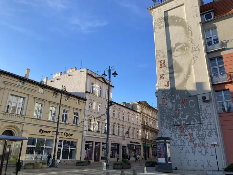 A sunny street scene in Krakow, Poland, featuring a large mural.