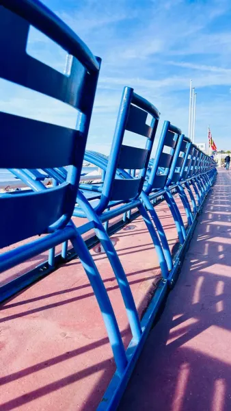 Blue chairs line a promenade in Nice, France, casting long shadows.