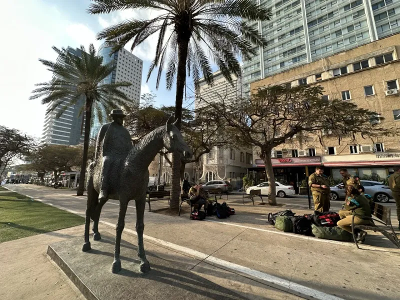 Bronze statue of a man on horseback in Tel Aviv, surrounded by palm trees and modern buildings.