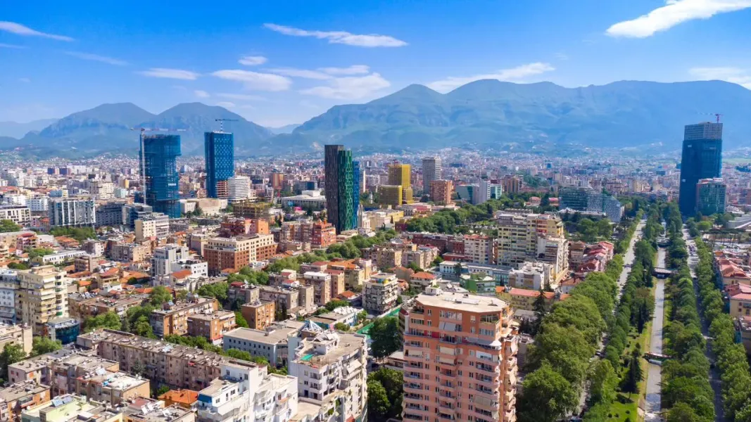 Aerial view of Tirana, Albania, showcasing modern skyscrapers and traditional buildings against a mountain backdrop.