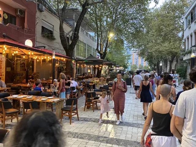 Bustling city street at night with outdoor restaurants and pedestrians.