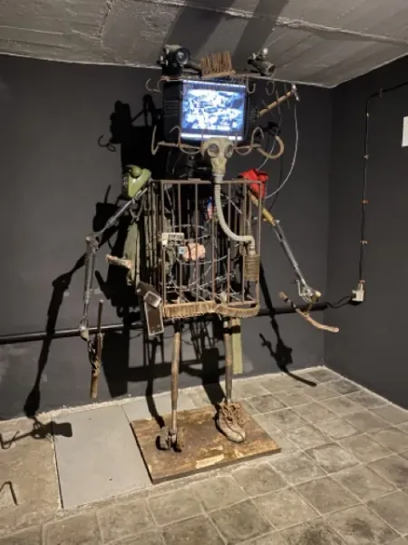 A captivating metal sculpture resembling a caged robot, displayed in a dark gallery.