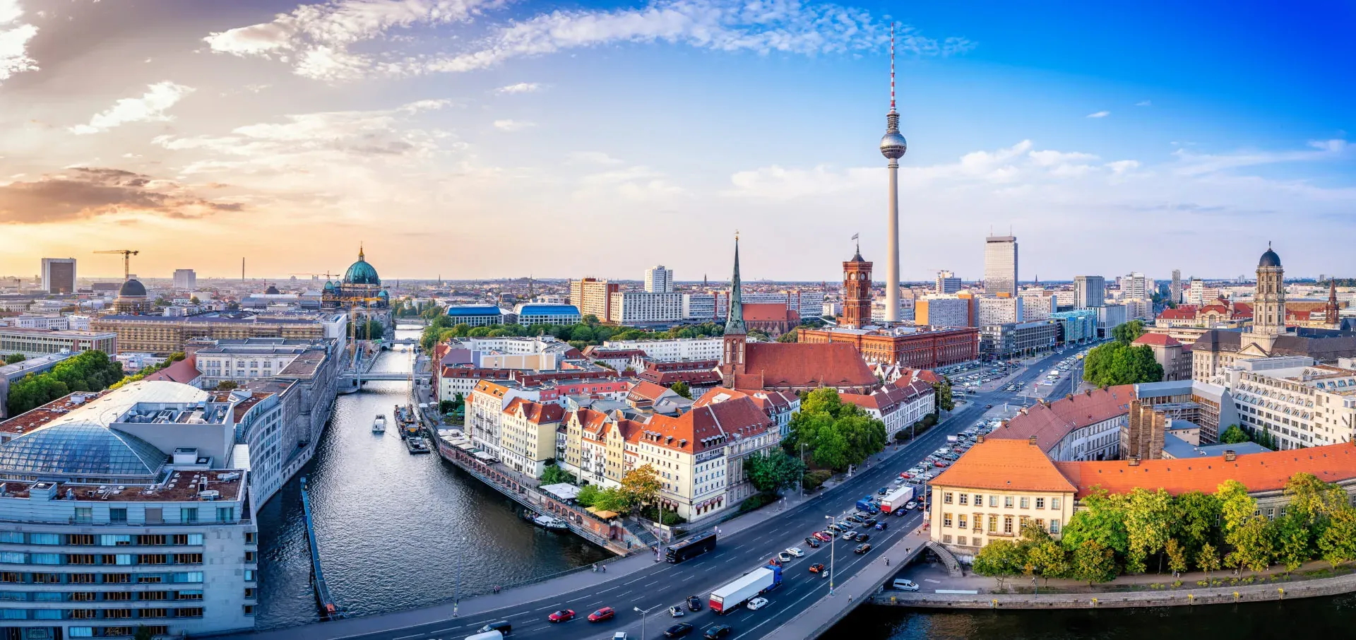 Panoramic view of Berlin's city center with the TV Tower, Berlin Cathedral, and the River Spree at sunset.