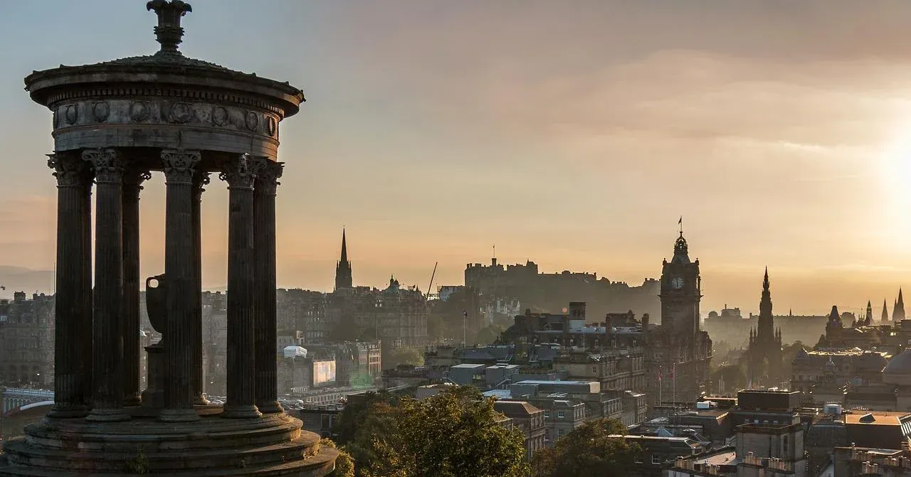 The Dugald Stewart Monument in Edinburgh's Calton Hill at sunrise, overlooking the city skyline with castle and monuments.