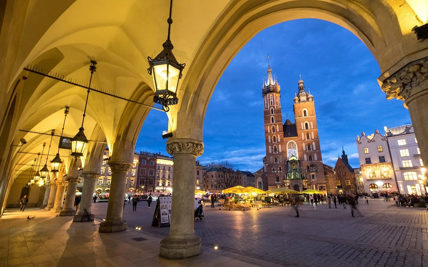 View of St. Mary's Basilica and Krakow Main Market Square at dusk, seen through the illuminated arches of the Sukiennice Clot