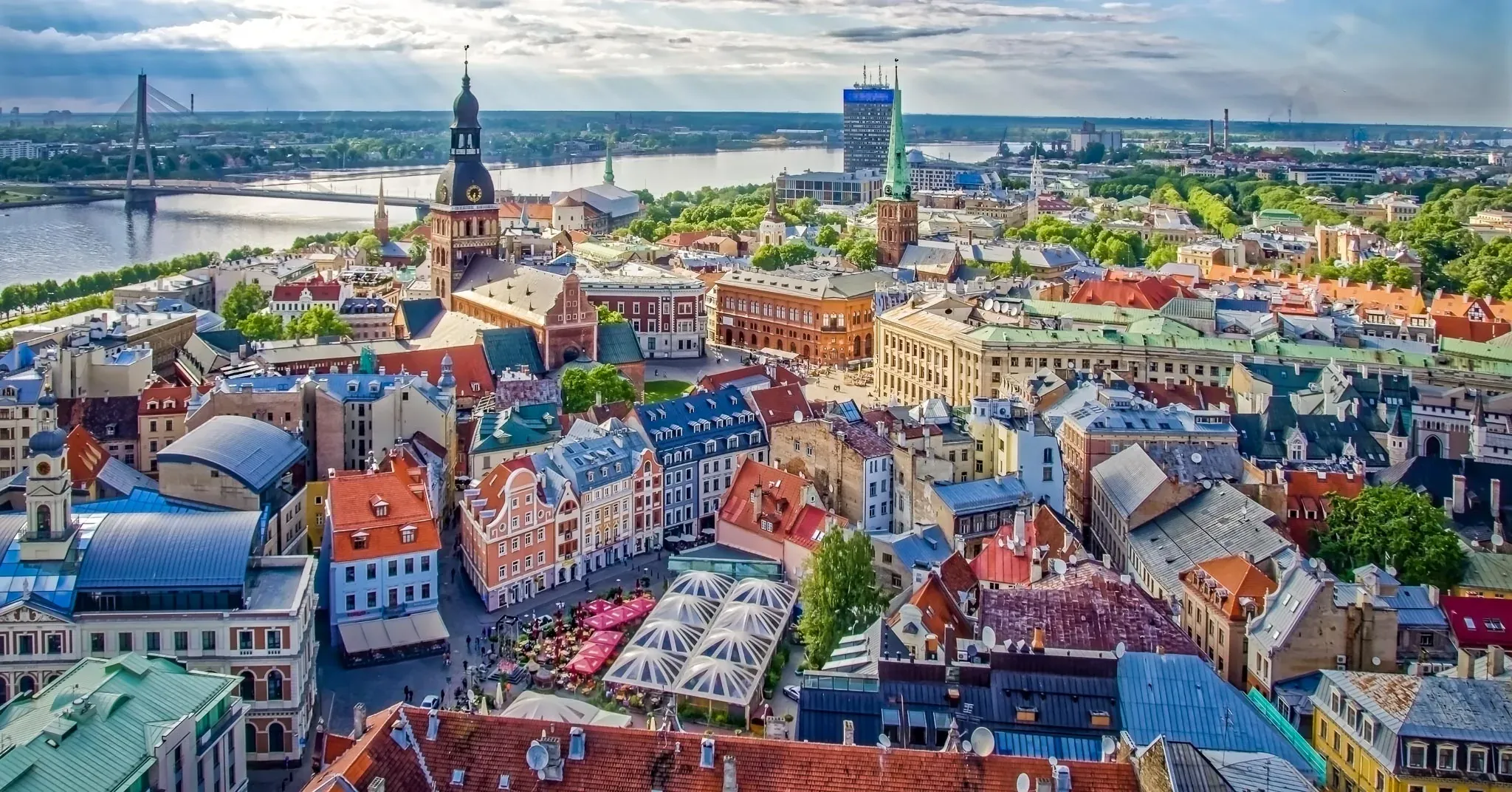 Aerial view of Riga Old Town with colorful buildings, St. Peter's Church spire, Daugava River, and Vansu Bridge under a cloud