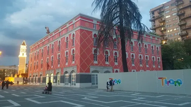 Tourists exploring a vibrant pink building and clock tower in Tirana, Albania.